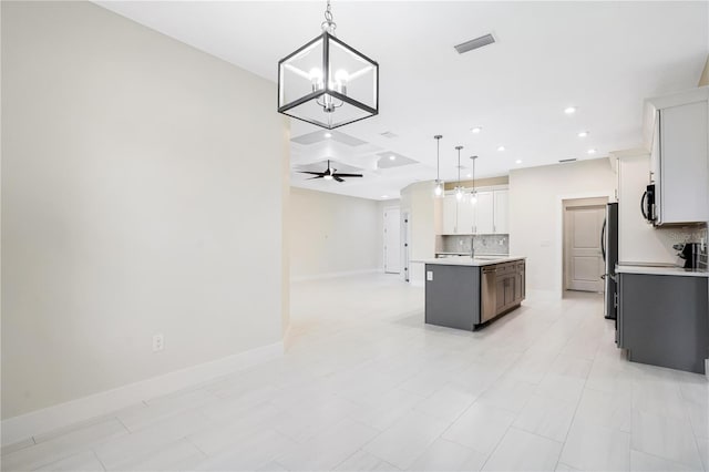 kitchen featuring white cabinetry, tasteful backsplash, ceiling fan with notable chandelier, a center island with sink, and pendant lighting