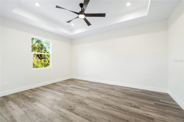 empty room featuring wood-type flooring, ceiling fan, and a tray ceiling