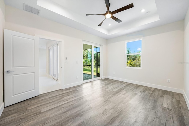 spare room featuring light wood-type flooring, ceiling fan, and a tray ceiling