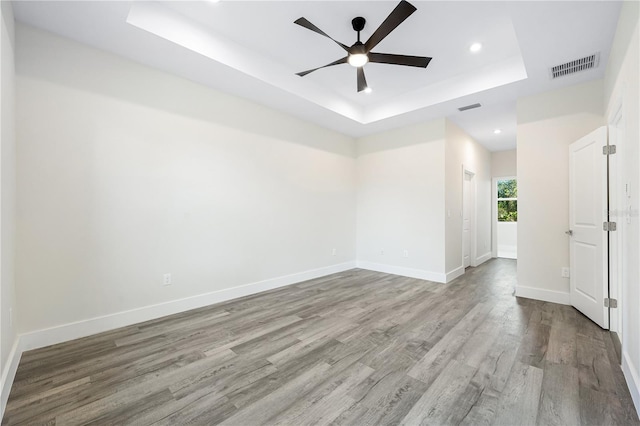 unfurnished room featuring a raised ceiling, light wood-type flooring, and ceiling fan