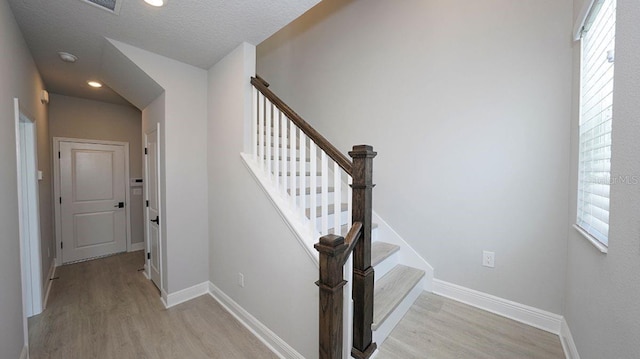 stairs with wood-type flooring and a textured ceiling