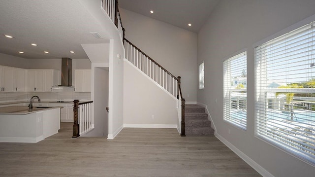 interior space with light hardwood / wood-style floors, white cabinetry, backsplash, and wall chimney exhaust hood