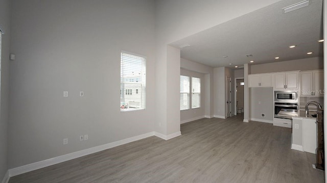 kitchen with sink, light wood-type flooring, appliances with stainless steel finishes, and white cabinetry