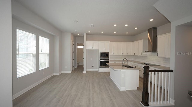 kitchen featuring wall chimney exhaust hood, stainless steel appliances, a kitchen island with sink, white cabinetry, and sink