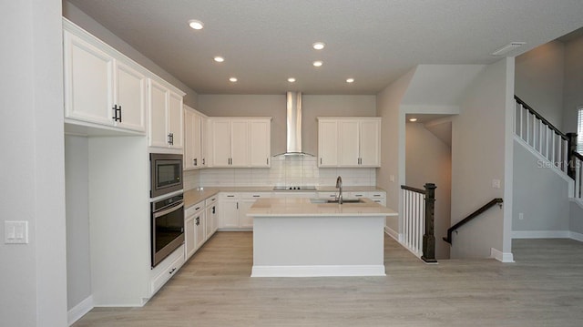 kitchen with stainless steel appliances, wall chimney range hood, tasteful backsplash, a kitchen island with sink, and white cabinets