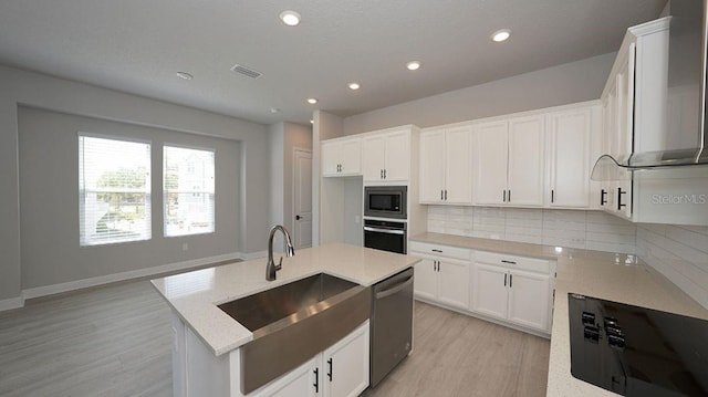 kitchen featuring stainless steel appliances, an island with sink, decorative backsplash, white cabinets, and sink