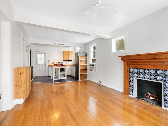 unfurnished living room featuring a tile fireplace, beam ceiling, light hardwood / wood-style floors, and ceiling fan