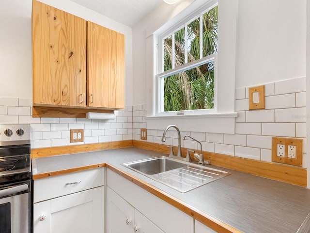 kitchen featuring backsplash, white cabinets, sink, and stainless steel stove