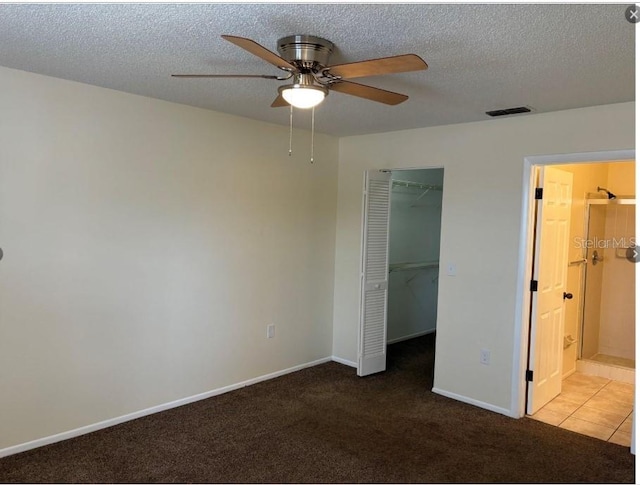 unfurnished bedroom featuring ceiling fan, a spacious closet, a textured ceiling, light carpet, and a closet