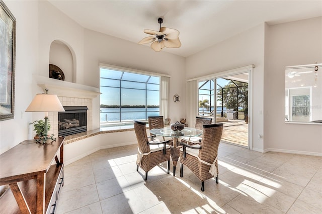 dining room featuring ceiling fan, a fireplace, a water view, and a healthy amount of sunlight