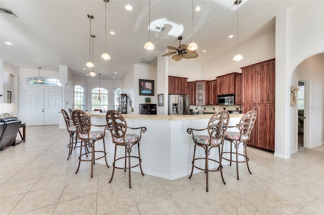 kitchen with a breakfast bar area, appliances with stainless steel finishes, ceiling fan, a spacious island, and hanging light fixtures