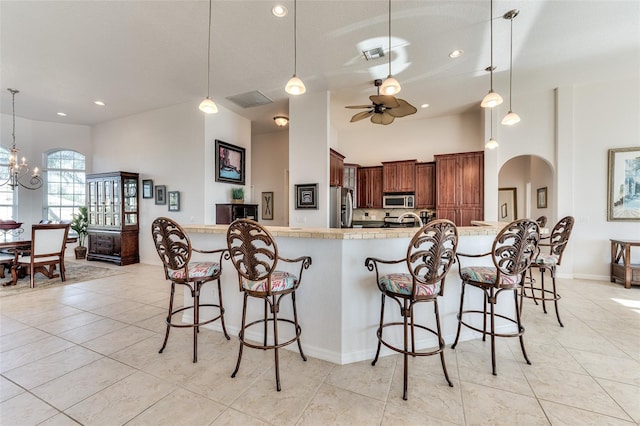 kitchen with ceiling fan with notable chandelier, pendant lighting, stainless steel appliances, light tile patterned flooring, and a breakfast bar area