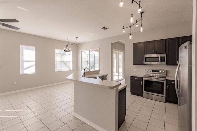 kitchen with sink, a center island with sink, light tile patterned floors, ceiling fan with notable chandelier, and appliances with stainless steel finishes