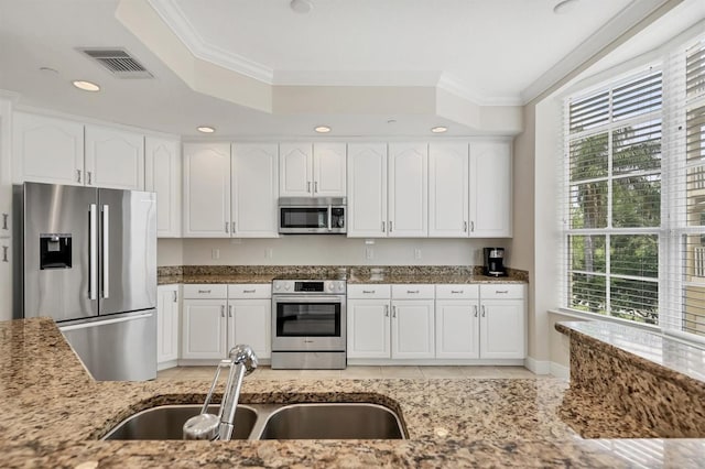 kitchen with appliances with stainless steel finishes, a sink, light stone countertops, ornamental molding, and white cabinetry