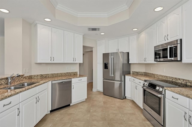 kitchen featuring stainless steel appliances, a sink, a raised ceiling, white cabinets, and crown molding