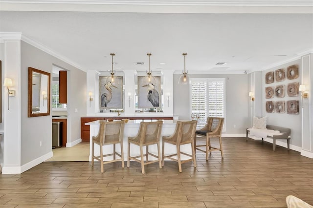 kitchen with light countertops, ornamental molding, a kitchen bar, baseboards, and decorative light fixtures