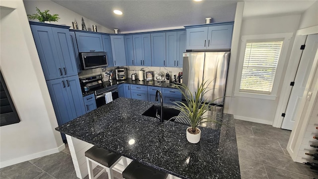 kitchen with appliances with stainless steel finishes, blue cabinetry, a kitchen breakfast bar, dark stone counters, and vaulted ceiling