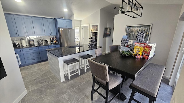 kitchen featuring a center island with sink, a breakfast bar, sink, stainless steel refrigerator, and blue cabinets