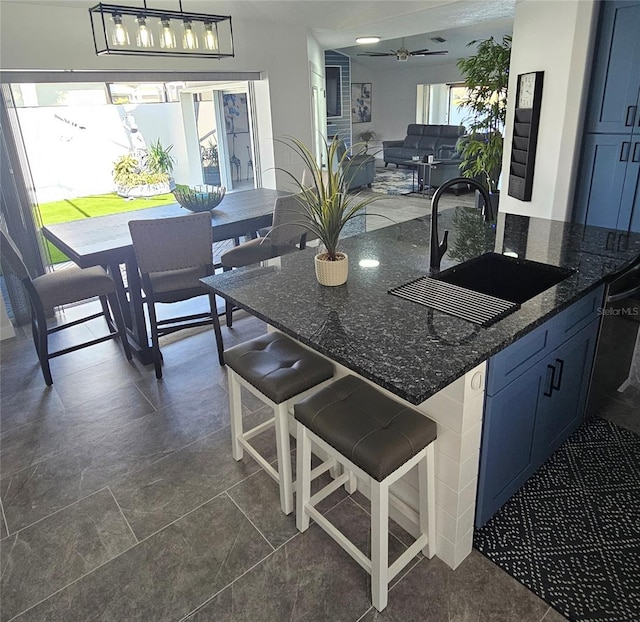 kitchen with blue cabinets, a breakfast bar area, dark stone counters, and a sink