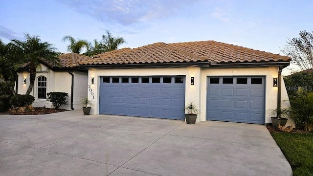 mediterranean / spanish-style home featuring a garage, driveway, a tiled roof, and stucco siding