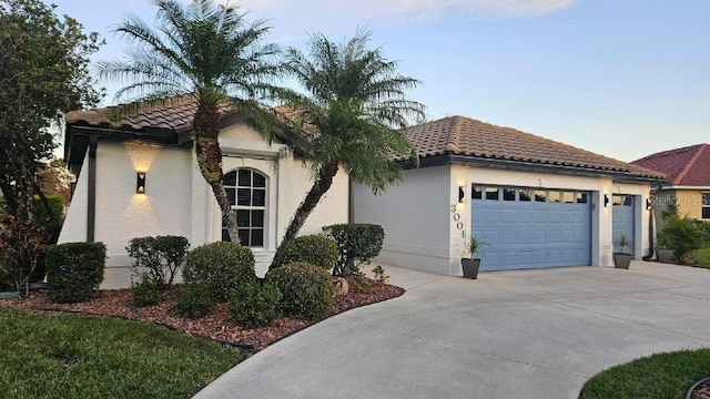 mediterranean / spanish-style home with a garage, a tiled roof, driveway, and stucco siding