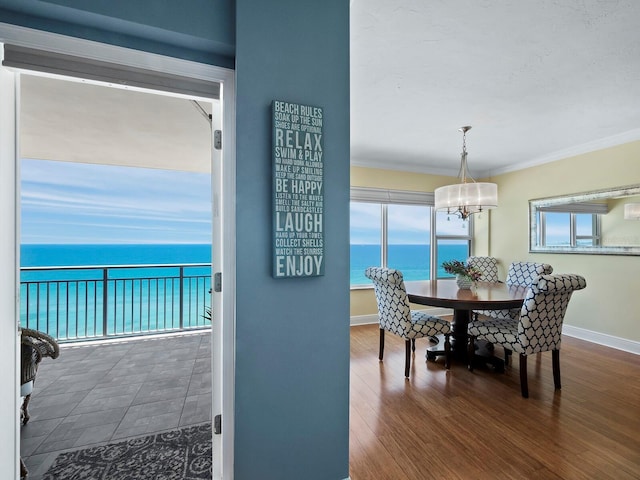 dining space with a chandelier, dark hardwood / wood-style flooring, a water view, and ornamental molding