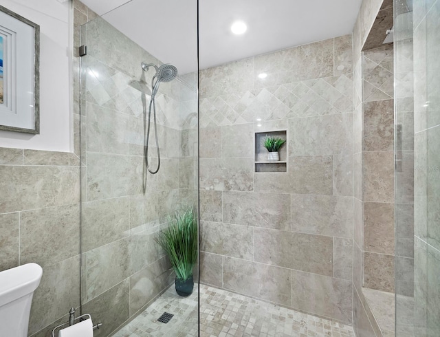 bathroom featuring tiled shower, toilet, and tile walls