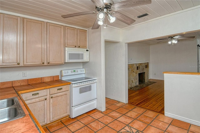 kitchen featuring a stone fireplace, tile counters, light brown cabinets, white appliances, and sink