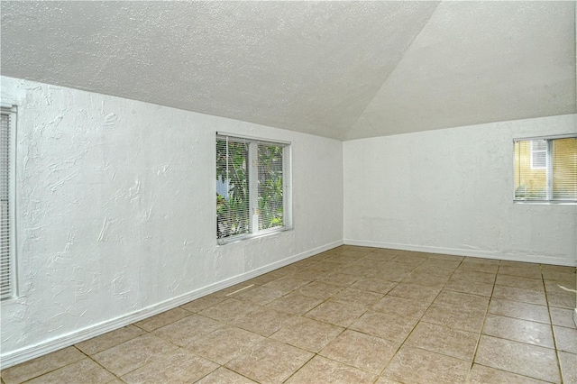 spare room with a textured ceiling, light tile patterned floors, and lofted ceiling