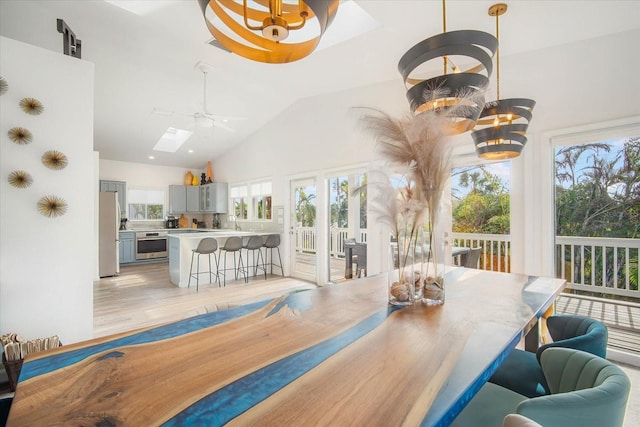 dining space featuring ceiling fan, lofted ceiling with skylight, and light wood-type flooring