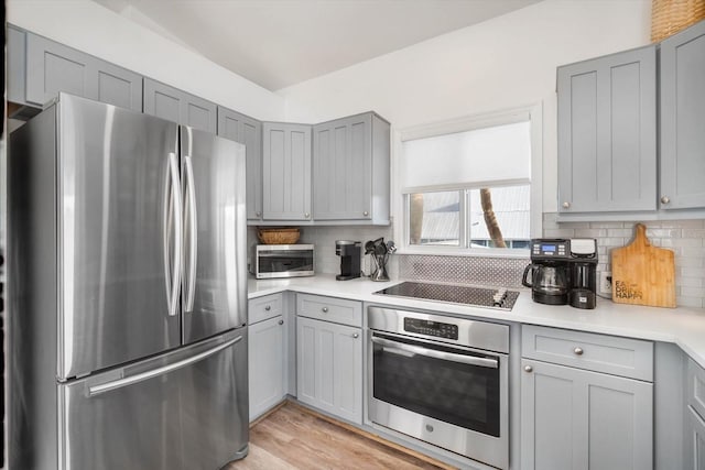 kitchen featuring appliances with stainless steel finishes, light hardwood / wood-style floors, gray cabinets, and decorative backsplash