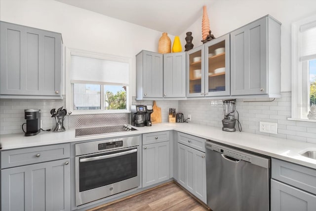 kitchen featuring a wealth of natural light, stainless steel appliances, light hardwood / wood-style floors, tasteful backsplash, and gray cabinetry