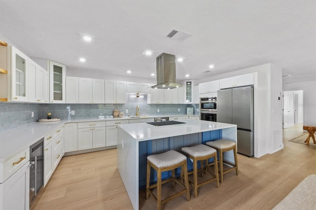 kitchen with sink, a center island, island exhaust hood, white cabinets, and appliances with stainless steel finishes