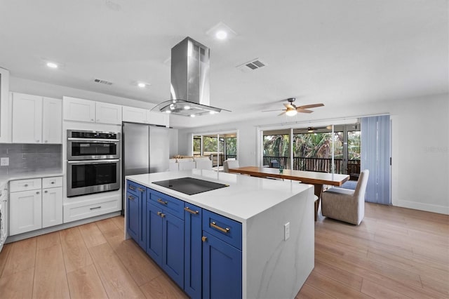 kitchen with island exhaust hood, black electric stovetop, stainless steel double oven, blue cabinets, and white cabinetry