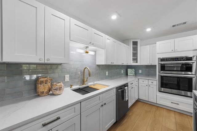 kitchen featuring white cabinets, sink, light wood-type flooring, black dishwasher, and tasteful backsplash