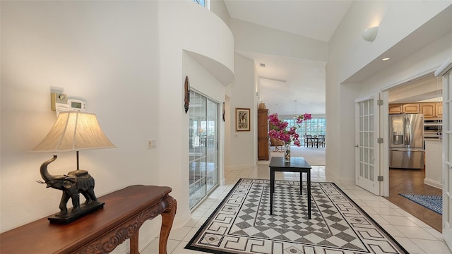 hall with a towering ceiling, a healthy amount of sunlight, and light tile patterned flooring