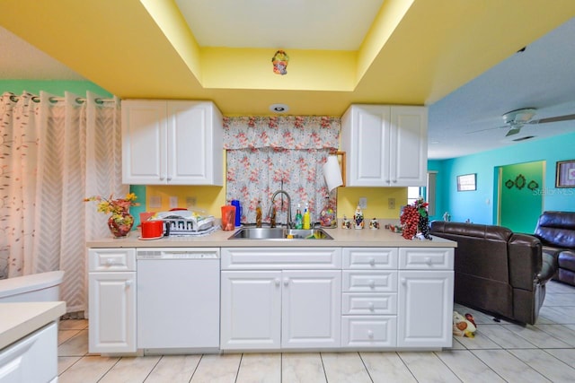 kitchen with light tile patterned floors, white dishwasher, a tray ceiling, white cabinets, and sink