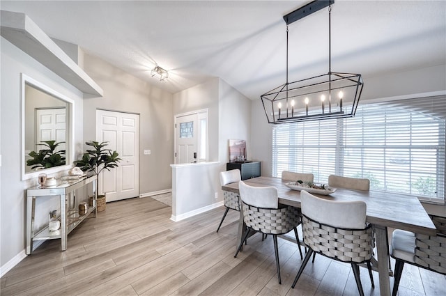 dining area with lofted ceiling, a notable chandelier, and light wood-type flooring