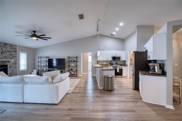 living room featuring vaulted ceiling, ceiling fan, light hardwood / wood-style floors, and a fireplace