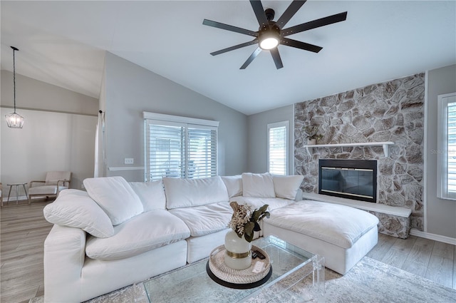 living room featuring ceiling fan, lofted ceiling, a stone fireplace, and light wood-type flooring