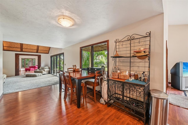 dining space with lofted ceiling, a textured ceiling, and hardwood / wood-style flooring