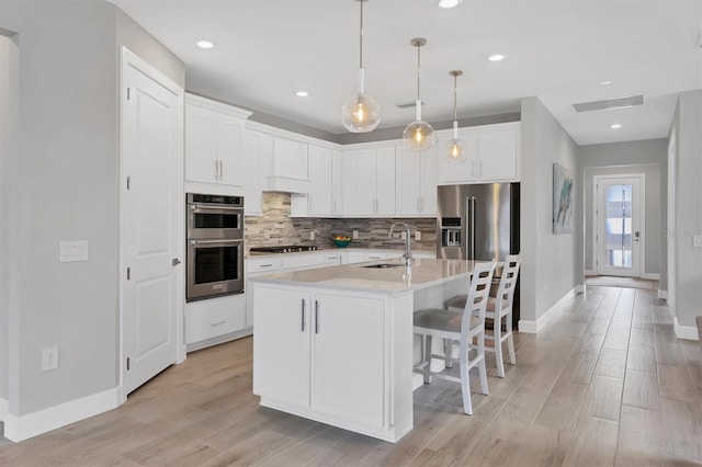 kitchen featuring appliances with stainless steel finishes, white cabinetry, sink, hanging light fixtures, and a kitchen island with sink