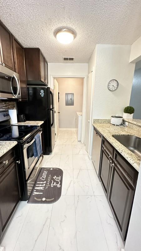 kitchen featuring dark brown cabinets, light stone countertops, separate washer and dryer, and appliances with stainless steel finishes