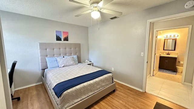 bedroom with ceiling fan, sink, ensuite bathroom, a textured ceiling, and light wood-type flooring