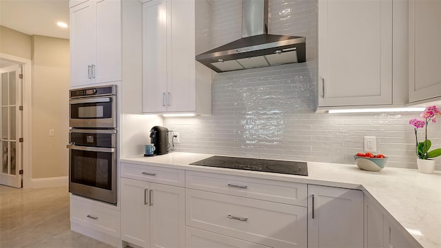 kitchen featuring light stone countertops, white cabinetry, wall chimney range hood, black electric stovetop, and double oven