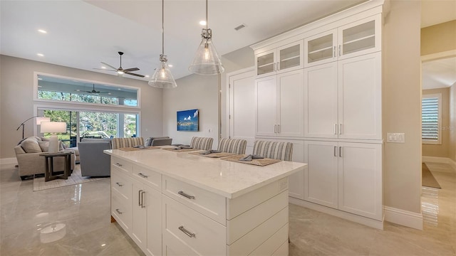 kitchen featuring light stone countertops, hanging light fixtures, white cabinets, and a kitchen island