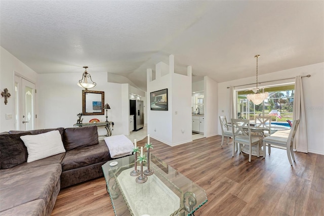 living room featuring lofted ceiling, sink, light wood-type flooring, a textured ceiling, and a chandelier