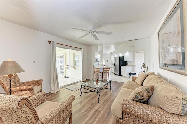 living room with ceiling fan, light wood-type flooring, and a textured ceiling