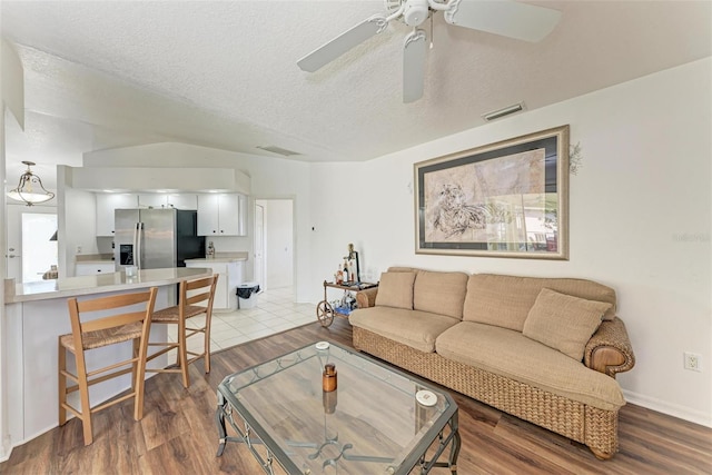 living room with ceiling fan, a textured ceiling, and light wood-type flooring