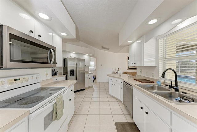 kitchen featuring white cabinetry, sink, stainless steel appliances, lofted ceiling, and light tile patterned floors